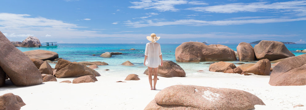 Woman wearing white loose tunic over bikini and beach hat on Anse Lazio beach on Praslin Island, Seychelles. Summer vacations on picture perfect tropical beach concept.