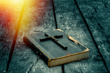 Closeup of wooden Christian cross on bible on the old table. Church utensils.