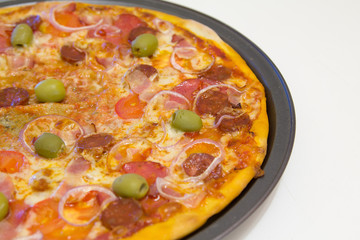 Pizza with chorizo, salami, bacon, onions and olives on a white wooden table, selective focus