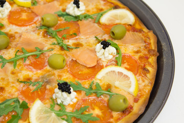 Pizza with salmon, olives, arugula and lemon on a white wooden table, selective focus