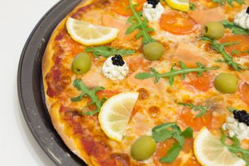 Pizza with salmon, olives, arugula and lemon on a white wooden table, selective focus