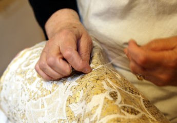 hands of the elderly while embroidering a lace with lace pillow