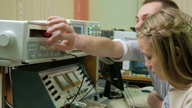 Young woman engineer student working with a man in the laboratory with an electrical measuring equipment. They carefully rotate the clock and recorded data