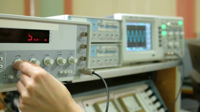 Young woman engineer student working in the lab with electric instrumentation. She carefully turns the wheel clock and looking for indications