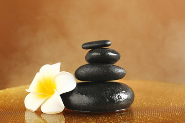 Spa stones with plumeria flower on color background