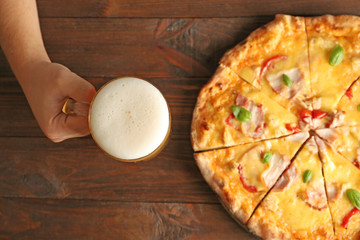 Man holding glass of beer and tasty pizza on table