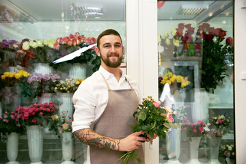 Handsome florist with bouquet near flower shop