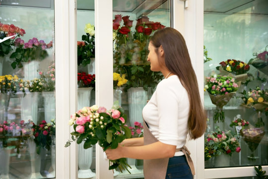 Pretty young florist with bouquet near flower shop