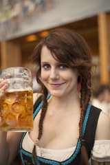 Portrait of cheerful young German woman wearing traditional dirndl and holding a beer mug inside a tent at Oktoberfest