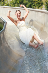 Junge Braut im Hochzeitskleid hat Spaß Ihr Kleid in einer Wasserrutsche zu schroten.
