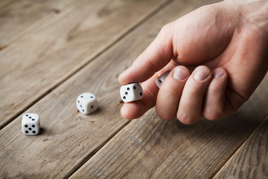 Man hand throwing white dice on wooden table. Gambling devices. Game of chance concept.
