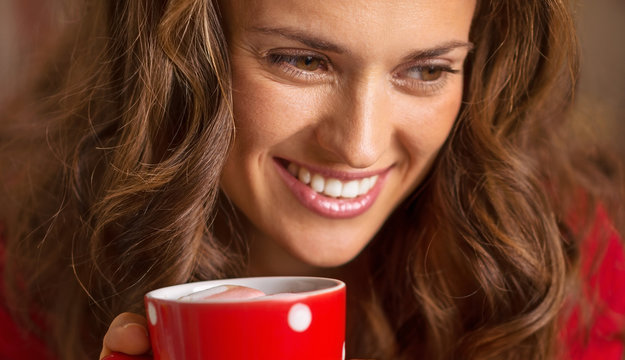 Happy young woman in christmas red dress having cup of hot bever