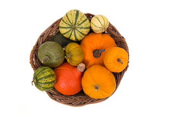 Brown wicker basket seen from above filled with green and orange pumpkins isolated on a white background