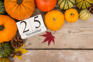 Date 25 november, thanksgiving surrounded with pumpkins and maple leaves on a white washed scaffolding wooden planks background