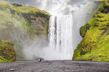 Two people lokking at spectacular Scogafoss waterfall in Iceland