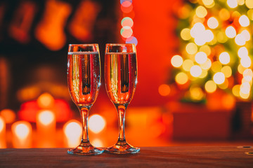 Beautiful two glasses of champagne standing on the table in the background of a blurred room with a decorated Christmas tree and fireplace. Soft focus. Shallow DOF