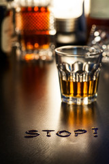 The word Stop on a bar with glass of alcohol in background