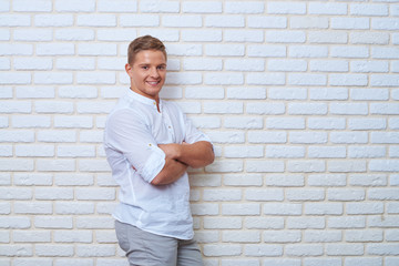 Positive young man keeping arms crossed and looking at camera wi