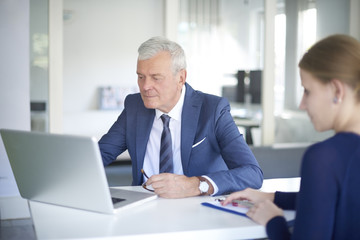 Financial team at work. Shot of a senior insurance agent consulting with her young client while sitting at office and working on laptop.