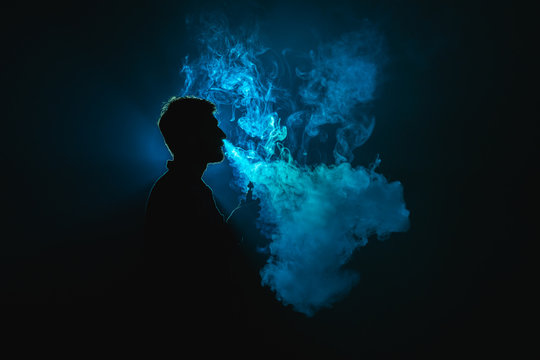 The man smoke a cigarette against the background of the blue light