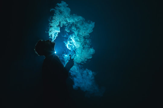 The young man smoke a cigarette against the background of the blue light