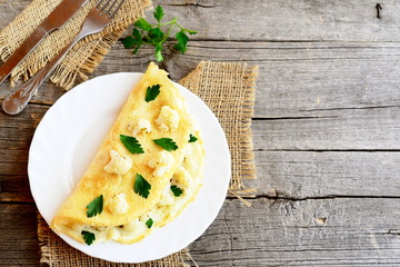 Cauliflower omelet decorated with parsley. Vegetarian omelet with cauliflower stuffing on a plate, fork and knife on old wooden background with blank space for text. Vintage style. Simple home cooking
