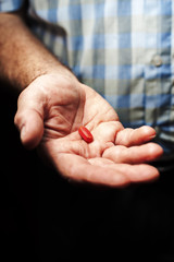 Closeup of senior male hand with medical red pill