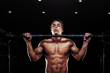 Young muscular man doing pull ups on bar.