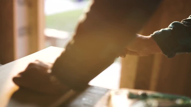 hand of a carpenter taking measurement of a wooden plank. sun flare ob background