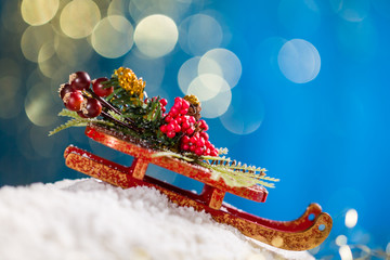 Sleigh with Christmas decoration on snow at blue background with gold glitter.