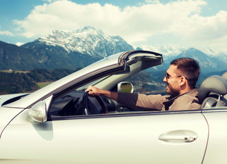 happy man driving cabriolet car over mountains