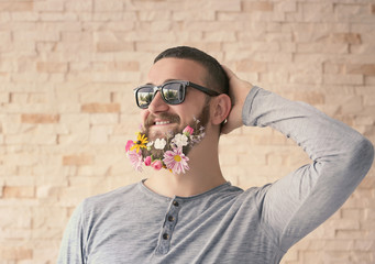 Handsome man in sunglasses with beard of flowers on light background