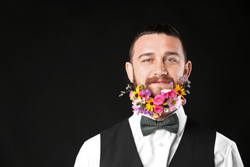 Handsome man with beard of flowers on dark background
