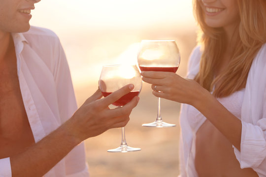 Young happy couple drinking red wine on seashore, closeup
