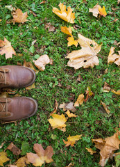 feet in boots and autumn leaves on grass