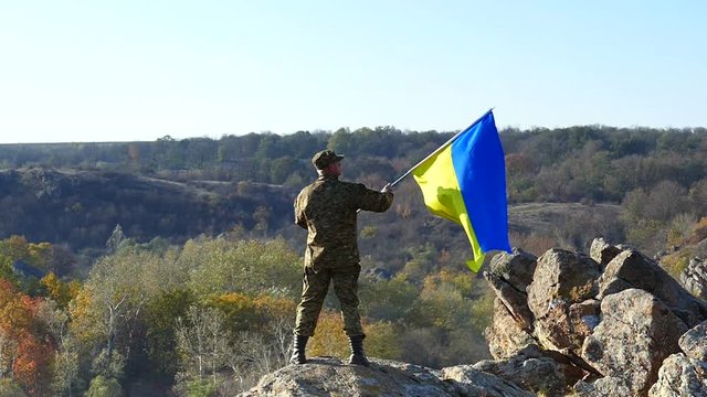 Soldier with Ukrainian Flag stand  at mountain top. Slow Motion 
