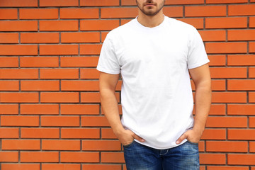 Young man in blank t-shirt standing against brick wall, closeup