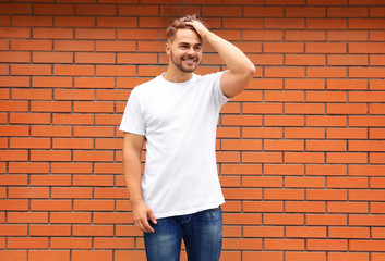 Young man in blank t-shirt standing against brick wall