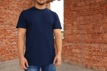 Young man in blank t-shirt standing near brick wall, closeup