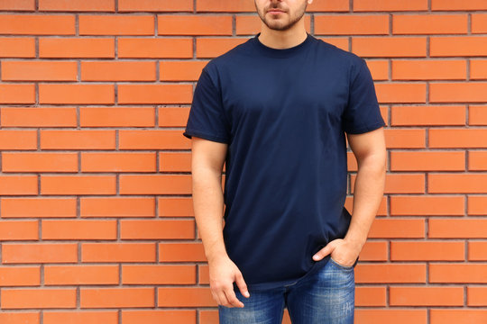 Young man in blank t-shirt standing against brick wall, closeup