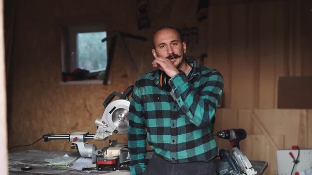 Portrait of a bold worker carpenter with vintage moustache in work clothes in front of workbench tools