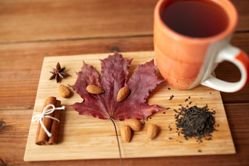 Fototapeta na wymiar cup of tea, maple leaf and almond on wooden board