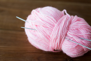 knitting needles and ball of pink yarn on wood