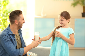 Father and daughter with glasses of fresh milk at living room