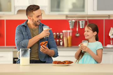 Father and daughter with glasses of fresh milk and buns at kitchen