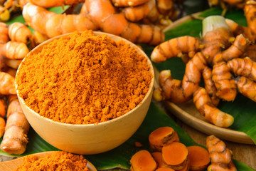 dry turmeric in a wood bowl  with leaf and fresh turmeric on tab