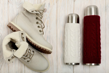 Fototapeta na wymiar Winter light boots and a thermos in the knitted cover on the bri