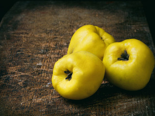 Three ripe yellow quince on a wooden background