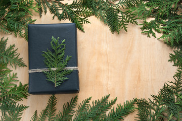 Christmas gift box wrapped in black paper with decor around branch cypress on wooden surface. Rustic style.