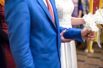 Bride and groom holds candles decorated wtih white flowers  ribbons